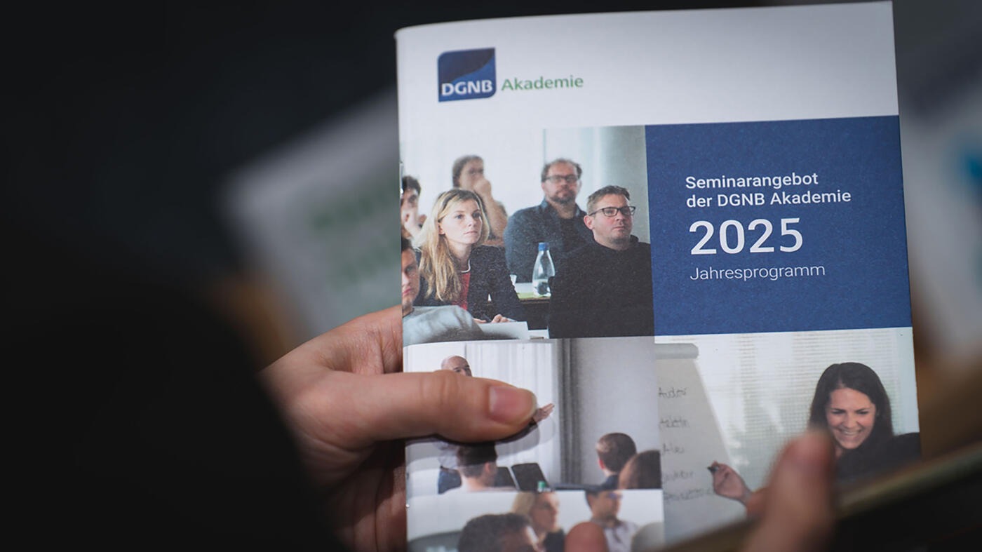 Das Seminarprogramm 2025 der DGNB Akademie, festgehalten von zwei Händen.