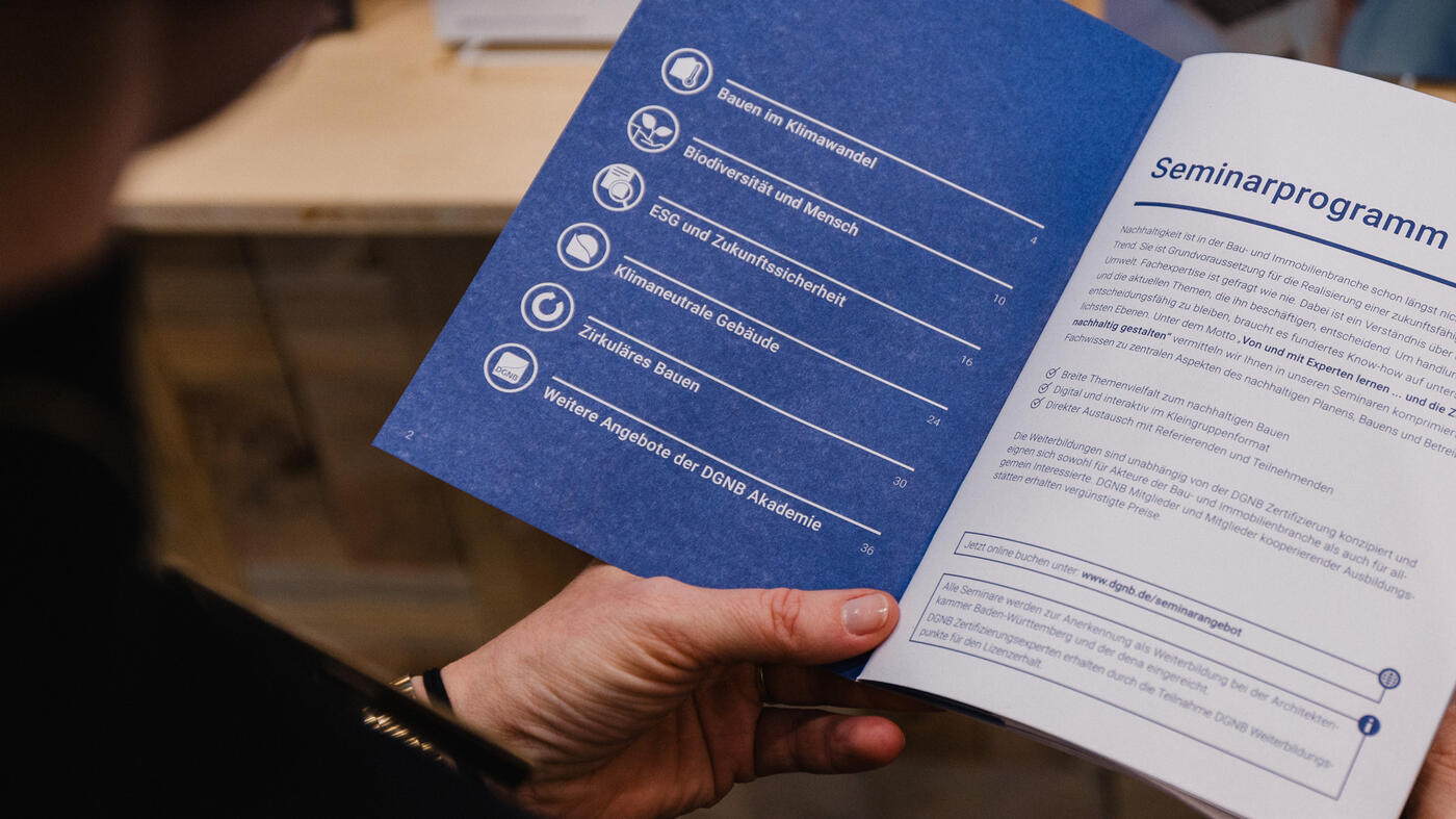Eine Hand hält das aufgeschlagene Seminarprogramm der DGNB Akademie.