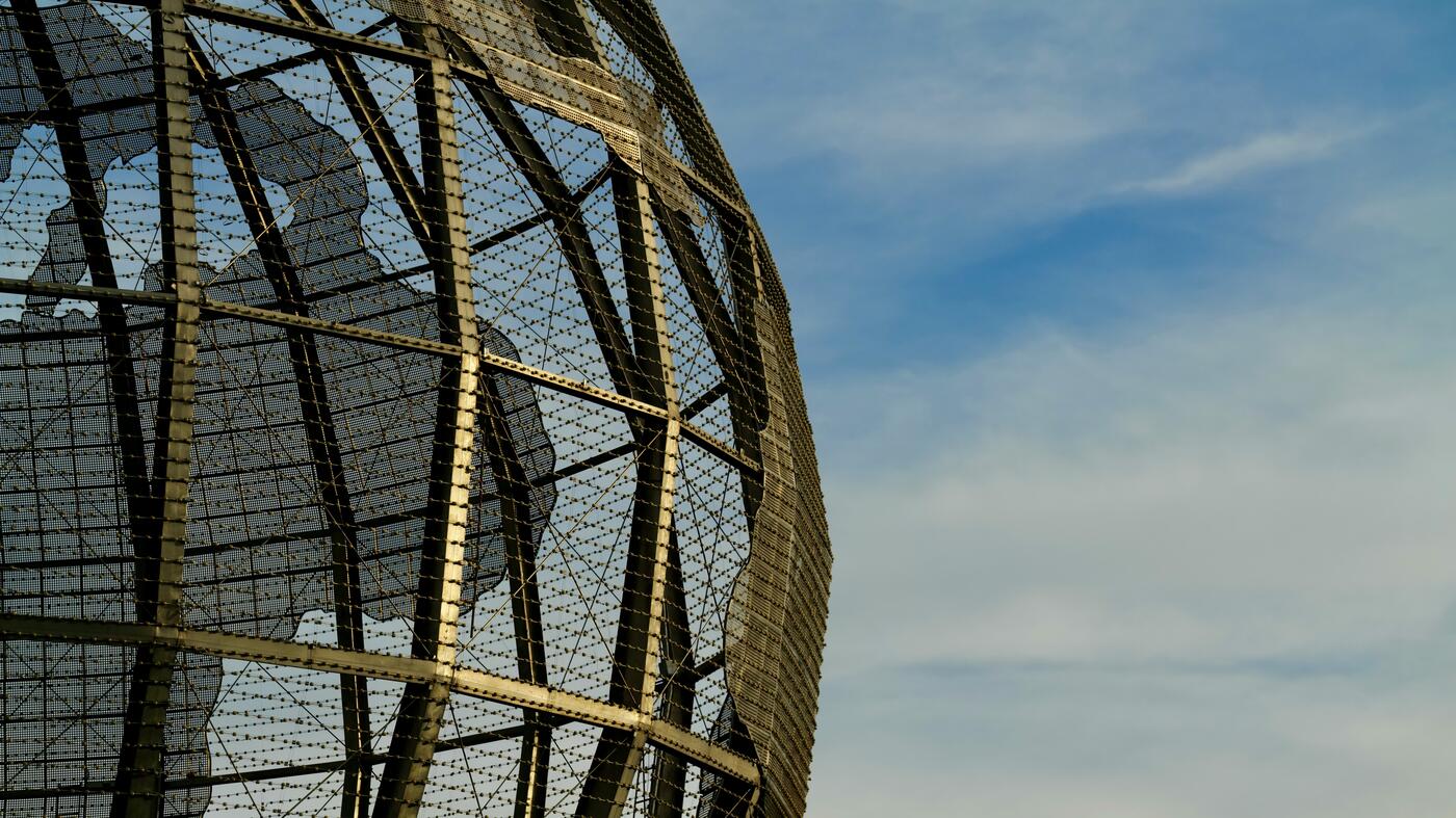 Drahtkonstruktion von Globus vor blauem, leicht bewölktem Himmel