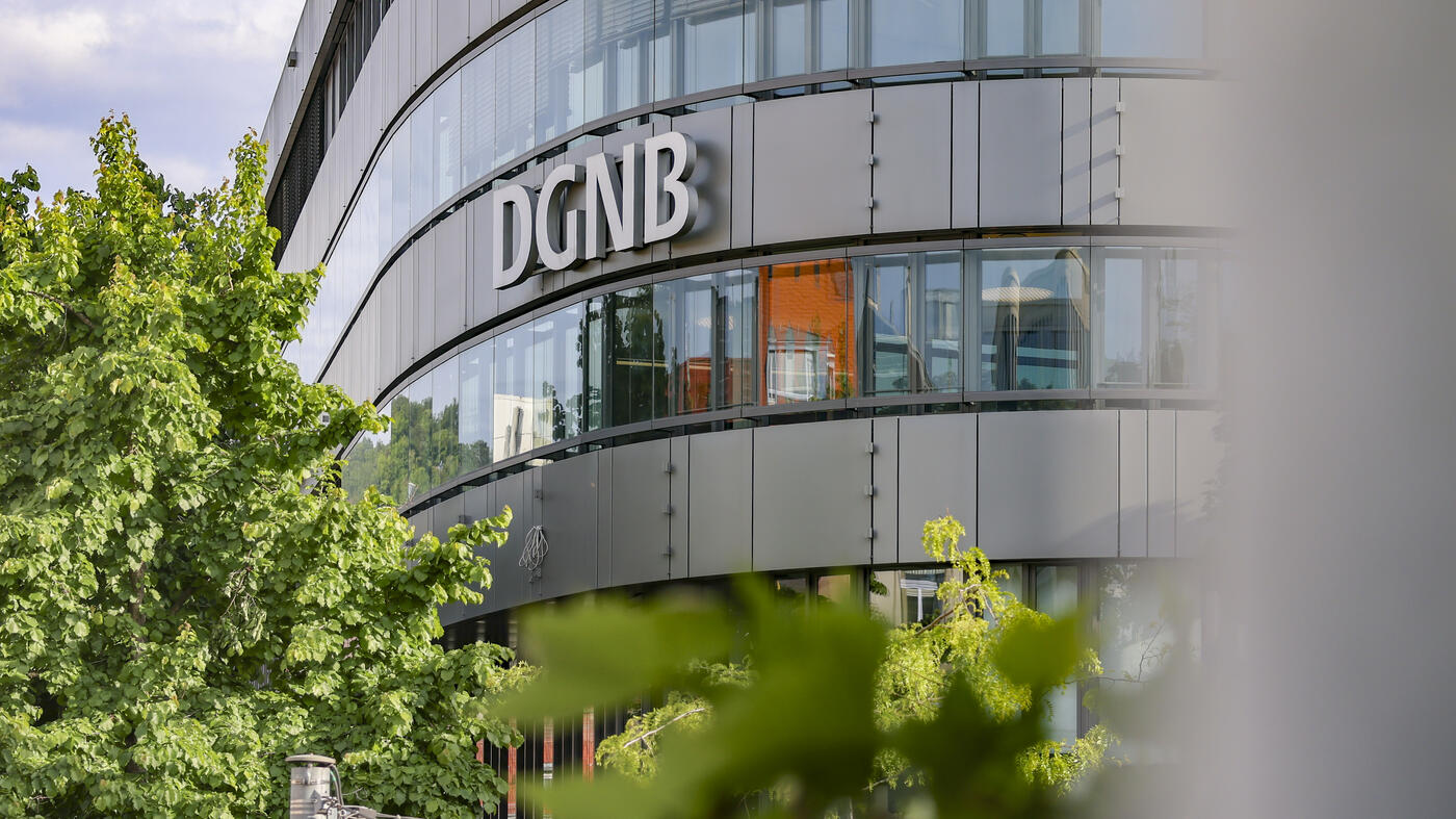 Aufnahme der DGNB Geschäftsstelle von außen mit Schriftzu an der Fassade und Baum in der unteren linken Bildecke