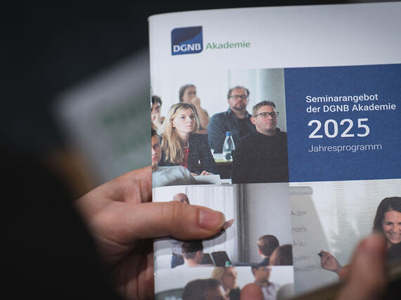 Das Seminarprogramm 2025 der DGNB Akademie, festgehalten von zwei Händen.