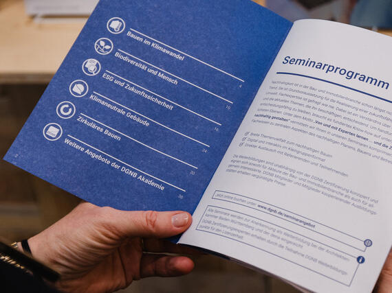 Eine Hand hält das aufgeschlagene Seminarprogramm der DGNB Akademie.