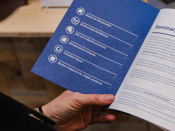 Eine Hand hält das aufgeschlagene Seminarprogramm der DGNB Akademie.