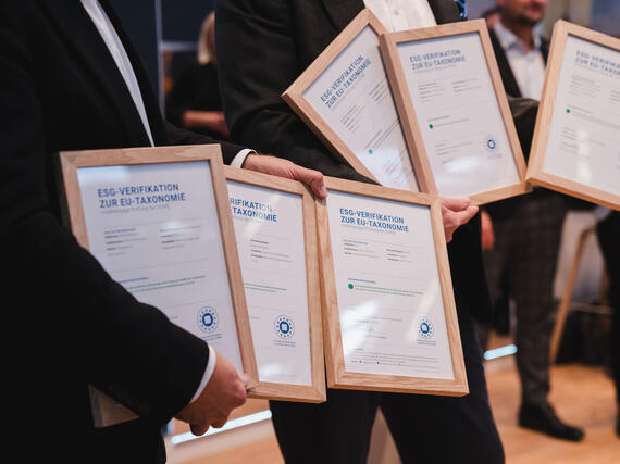 Personen halten gerahmte Auszeichnungen zur ESG-Verifikation zur EU-Taxonomie in den Händen.