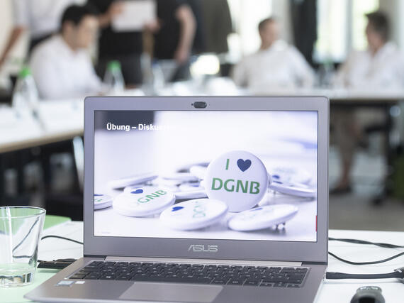 Aufgeklappter Laptop mit I love DGNB Buttons als Hintergrund