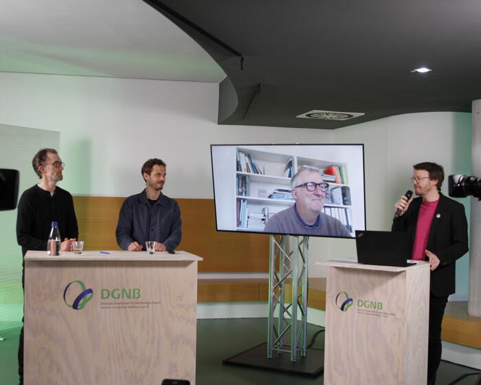 Zu sehen ist eine Studiosituation mit Kameras links und rechts. Im Zentrum des Fotos ist rechts Felix Jansen (DGNB) mit einem Mikrofon zu sehen. Links sind hinter einem Pult zu sehen: Kilian Juraschitz, Geschäftsführer, Atelier Kaiser Shen und Prof. Dr. Julian Lienhard, Geschäftsleitung / Partner, str.ucture GmbH. Auf einem Monitor in der Mitte ist zudem zu sehen: Markus Müller, Präsident, Architektenkammer Baden-Württemberg