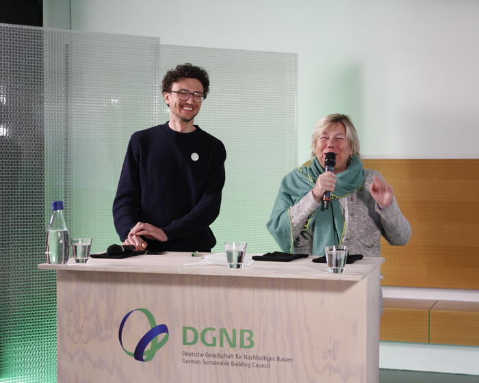 Zu sehen sind zwei Personen hinter einem Pult: Leon Beck, Vorstandsvorsitzender, Architects for Future Deutschland e.V. und Sylvia Pilarsky-Grosch, Landesvorsitzende, BUND Baden-Württemberg e.V. | Sylvia Pilarsky-Grosch hält ein Mikrofon in der Hand